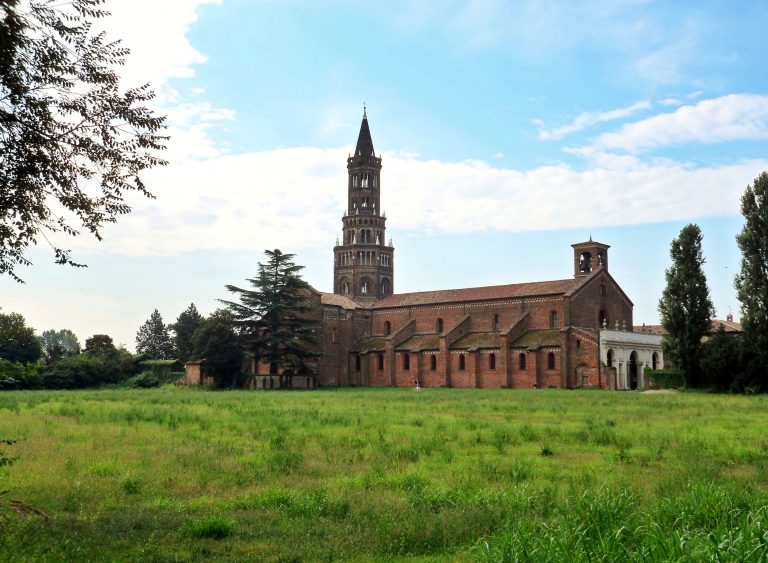 Abbazia di Chiaravalle a Milano, con la torre nolare e le mura in mattoni oltre un prato.